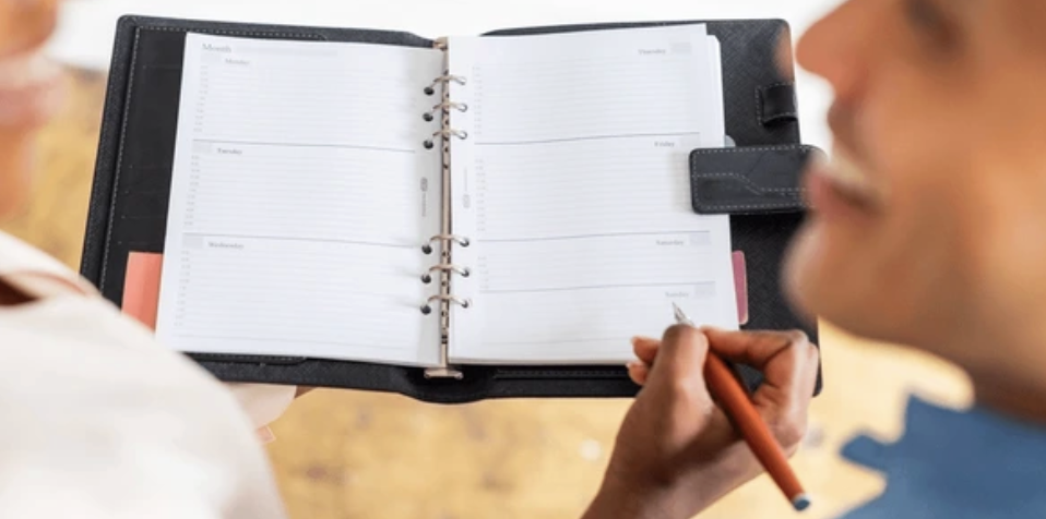 Two people looking at and writing in a planner held open in one hand.