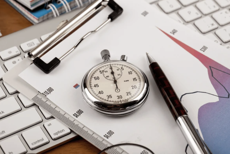 A stopwatch resting on a desk beside a pen and paper.